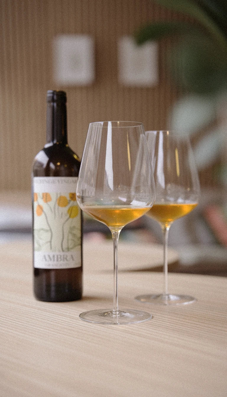 Två vinglas med en flaska orangevin bredvid